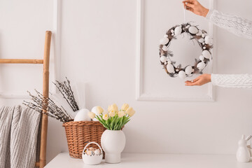 Female hands with Easter wreath near light wall in office