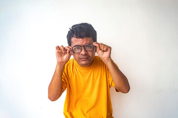 Fototapeta premium A man in a yellow shirt is excitedly adjusting his glasses with both hands against a plain white background. The image highlights his enthusiasm and clear action