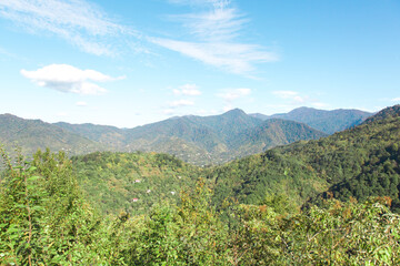 Mountainous landscape of Adjara with lush green hills, scattered houses, a bright blue sky with white clouds. The scenic view showcases beauty of Georgia's nature. Concept of travel, nature, tourism