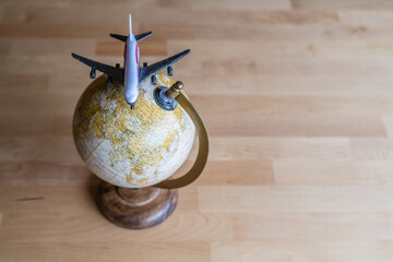 Miniature airplane model is positioned on top of a world globe resting on a wooden table, representing the concept of international travel and exploration