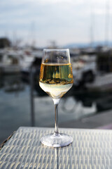 A glass of white wine rests on a textured table, with a blurred marina backdrop, suggesting a relaxing moment by the water.