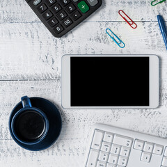 Phone With Important Message On Desk With Wood Tables And Clipboard. Cellphone Screen With Crutial Announcement. Calculator, keyboard, cup of coffee and pens.