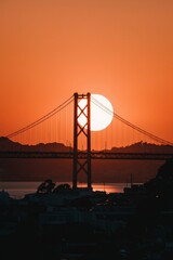 Obraz premium Suspension Bridge Silhouette at Sunset over Hills and City