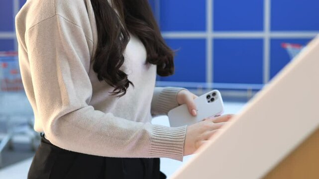 Woman is holding a white iPhone in her hand. She is wearing a white sweater and black pants