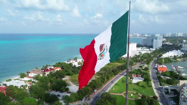 Mexican flag flying on a flagpole in the median of the Cancun Quintana Roo hotel zone, beautiful waves, sea and beach are seen in the background, as well as the Nichupt&eacute; lagoon on a beautiful day