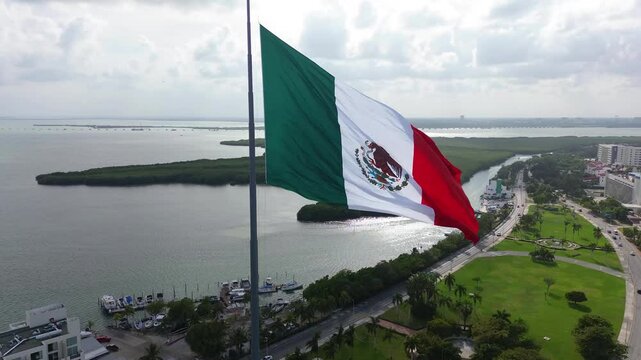 Mexican flag flying on a flagpole in the median of the Cancun Quintana Roo hotel zone, beautiful waves, sea and beach are seen in the background, as well as the Nichupt&eacute; lagoon on a beautiful day