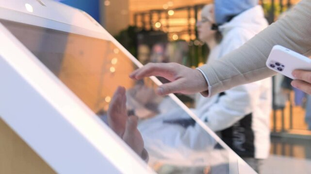 Person is touching a screen with a phone in their hand. Concept of technology and the way it has become an integral part of our daily lives. The person's interaction with the screen