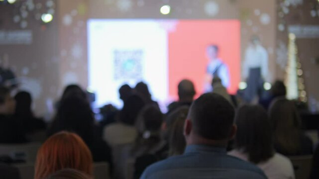 Man is giving a speech to a large audience. The audience is attentive and engaged. The speaker is using a projector to display his presentation