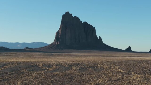 A low to the ground, slow-rising 70mm drone shot of the sacred &ldquo;Ship Rock&rdquo;, a massive, monolithic monadnock towering above the high-desert plain of the Navajo Nation, in New Mexico, United States.
