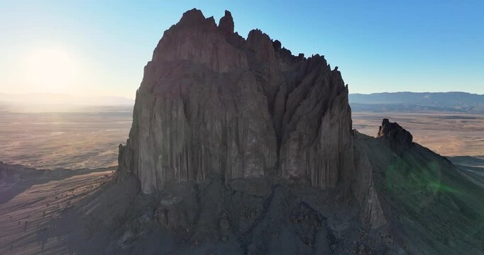 An unworldly, close-up orbital drone shot of the sacred &ldquo;Ship Rock&rdquo;, a massive, monolithic rock butte, towering above the high desert plain of the Navajo Nation, in New Mexico, as the sun sets behind.
