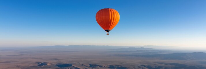 A hot air balloon is flying high in the sky above a desert landscape. The balloon is orange and can be seen against a blue sky. Concept of adventure and freedom, as the balloon soars above the vast