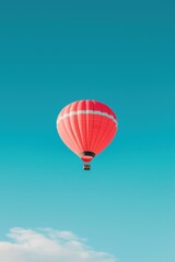 Fototapeta premium A red hot air balloon is floating in the sky above a blue sky. The balloon is the main focus of the image, and it is floating effortlessly, giving the impression of freedom and adventure