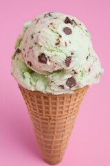 delicious ice cream cone with mint chocolate chips on a pink backdrop  
