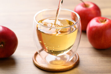 Apple cider pouring into glass with apple fruit on wooden background