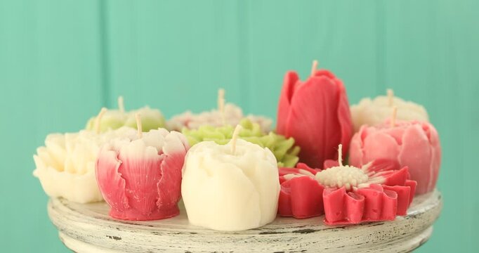 Beautiful flower shaped candles on white tray against turquoise background, closeup