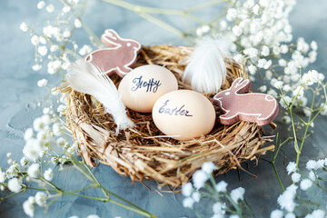 Two chicken eggs with the inscription Happy Easter in a nest of dry grass with feathers, rabbits...