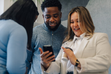 Smiling business team using smartphone and drinking coffee