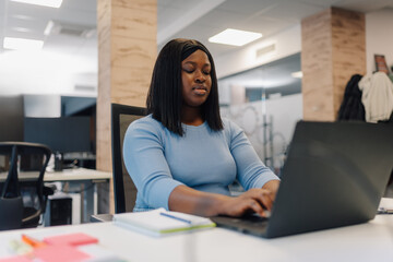 Fototapeta premium Focused female entrepreneur working on laptop in modern office