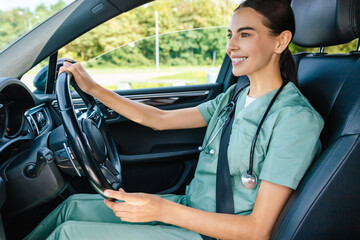 Smiling beaming young woman in scrub suit driving a car