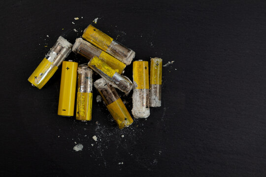 Oxidized and leaked AA alkaline batteries on dark surface. White powder Potassium hydroxide was formed by leakage of alkaline electrolyte. Hydroxides and carbonates are dangerous, powder caustic