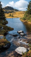 Serene mountain stream flows into a calm lake, surrounded by autumnal foliage and rocks under a partly cloudy sky.