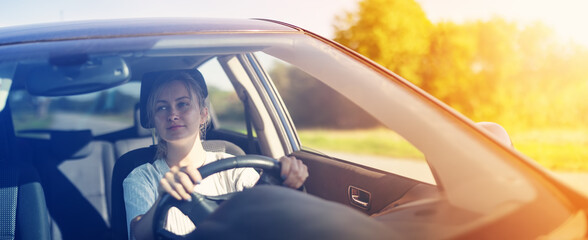 Young woman sitting behind the wheel and driving a car on a sunny day.