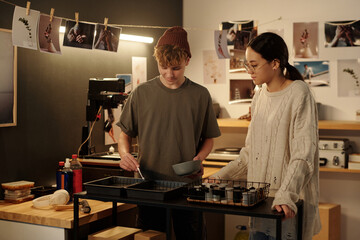 Portrait of teenage boy and girl working together developing photo prints in studio and mixing chemical solution in trays copy space