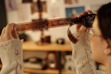 Close up of young teenage girl carefully holding film negatives to light while analyzing developed images in darkroom copy space