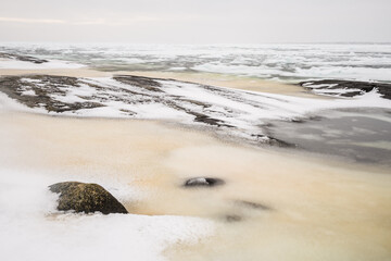 Winter sea ice envelops stone formations along the Swedish coast in a tranquil, icy landscape