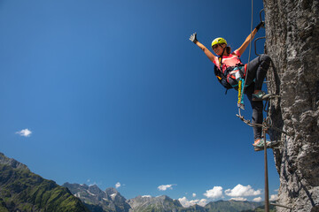 Pretty, female climber on a via ferrata - climbing on a rock in Swiss Alps