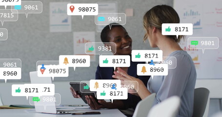 Image of social media icons with numbers over diverse colleagues discussing work in office