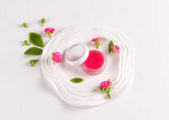 Cosmetic jar with pink lip balm on a white embossed tray with small Kalanchoe flowers. Natural lip skin care. top view. Daily lip care