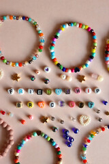 Friendship bracelet spelled with letter beads. Colorful handmade bracelets and various beads. Flat lay, pink background.