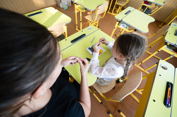 In a brightly lit classroom, a teacher guides a young student as they work with clay at a cheerful...