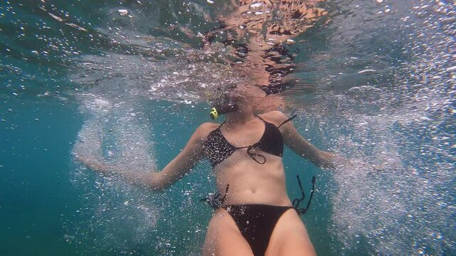 Woman snorkeler swimming underwater in crystal-clear turquoise water. Person wearing bright yellow diving mask and snorkel with black swimsuit. Camera fast going to her simulates a shark attack