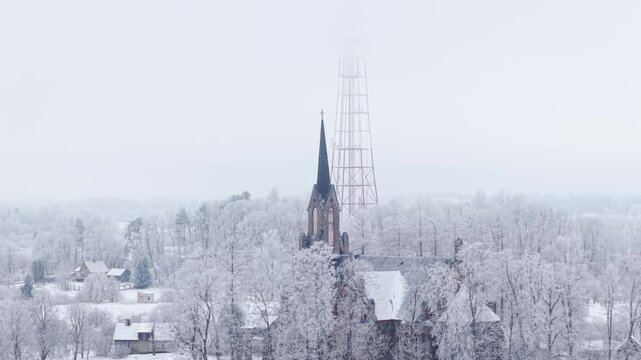 A tall radio communication tower emerges from dense fog, standing against the misty sky above old town