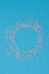 A top-down shot of numerous small, clear glass beads scattered around a circular empty space against a light blue background