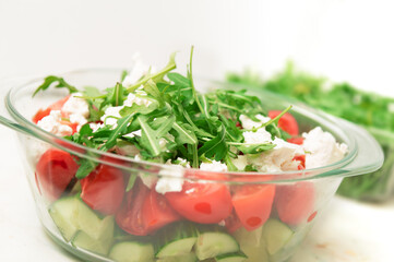 Fresh and healthy salad featuring tomatoes, cucumbers, feta, and arugula in a glass bowl. A bright, vibrant, and wholesome food image