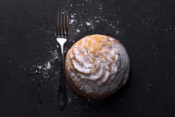 Close up of a cream bun dusted with icing sugar on a dark surface