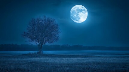 Fototapeta premium A large moon illuminates a field with a lone leafless tree