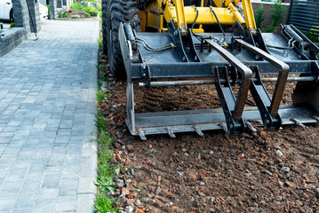 A backhoe loader carries and levels rubble on a dirt road.