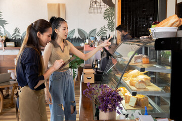 Asian cafe cashier worker female showing menu or cashless billing payment to customer, barista small business owner using technology tablet receives coffee order at workplace in restaurant coffee shop
