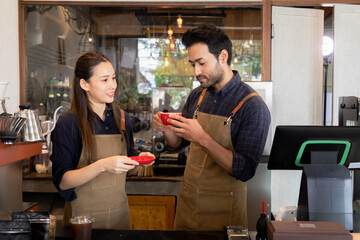 Cafe employees discuss while holding coffee cups. Smiling female barista in uniform talking with Indian entrepreneur or partnership enjoying coffee. Friendly interaction in cozy cafe small business