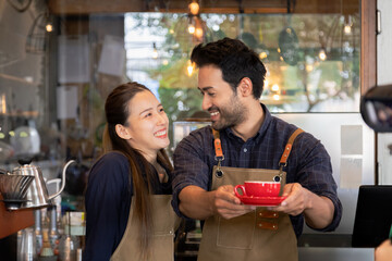 Cafe small business entrepreneur couple presenting coffee with red cup. Male and female baristas with aprons standing behind counter with coffee machines. startup restaurant owner in cozy workplace