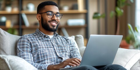 Relaxed Young Man Enjoying Online Content Smiling While Using Laptop on Comfortable Couch at Home