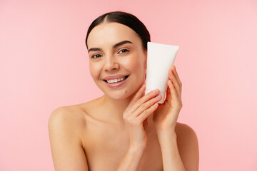Portrait of a smiling girl woman holding a cosmetic product, depicted against a charming pink...