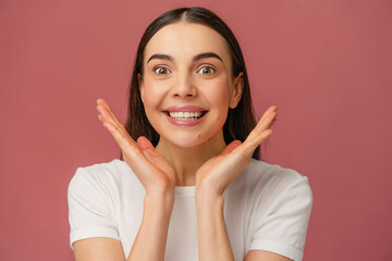 Bright and cheerful person smiling broadly with hands near face, captured against a pink background.