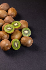 Fresh kiwi fruits displayed on dark background, showing whole and halved pieces