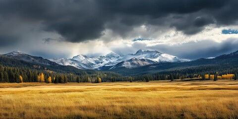 Paysage d'une prairie en automne, surplombée par de sombres nuages ​​d'orage, entourée de forêts et de montagnes enneigées, capturant une vue magnifique évoquant la grandeur et la beauté de la nature.