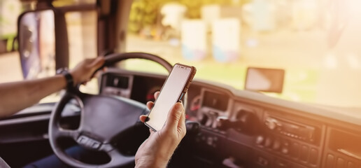 Truck driver sitting behind the wheel and looking at the smartphone.